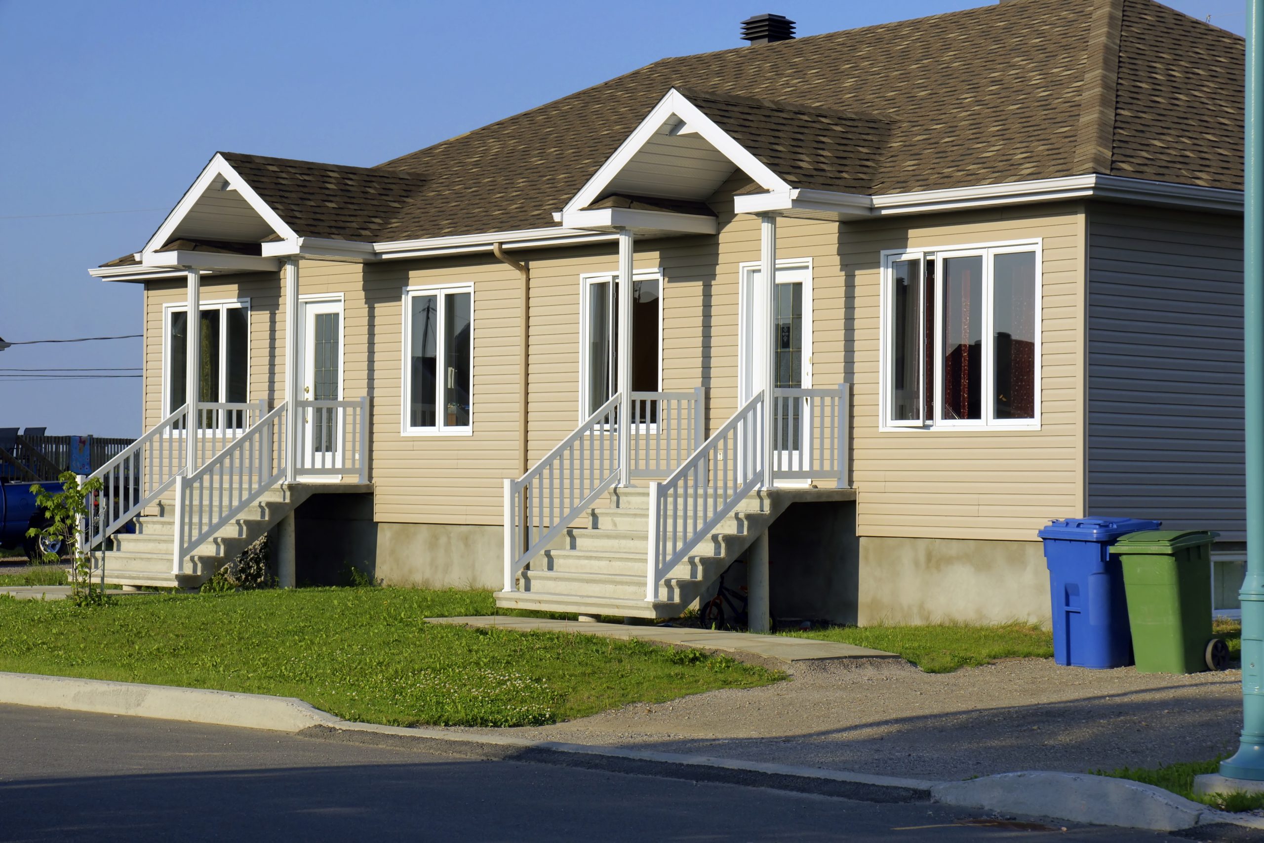 New construction and real estate: beige siding duplex house with recycling and garbage bins.